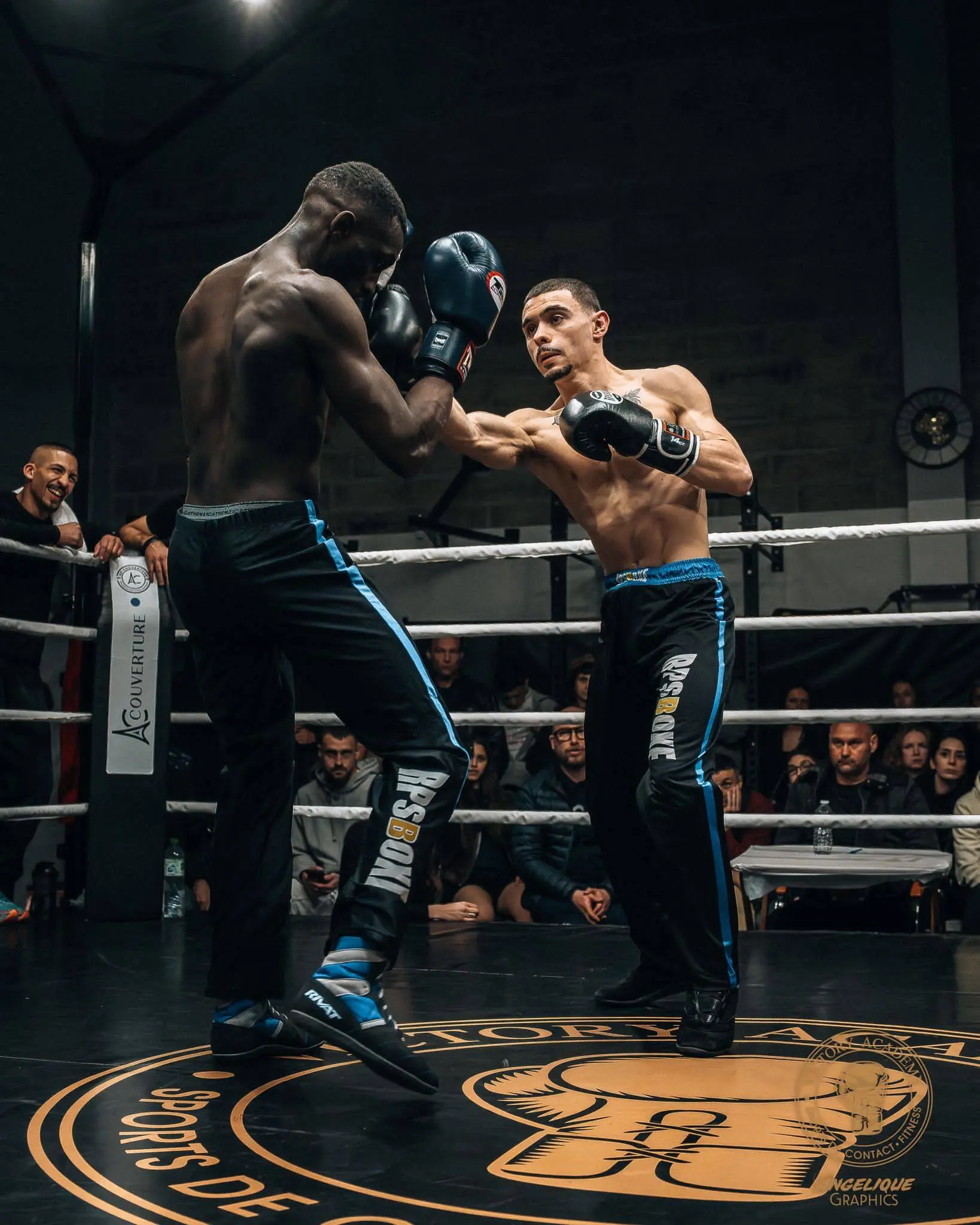 Deux boxeurs en plein combat dans un ring, l’un esquivant un coup porté par l’autre; spectateurs et panneaux autour du ring. Syndrome de la boxe évoqué dans le contexte.