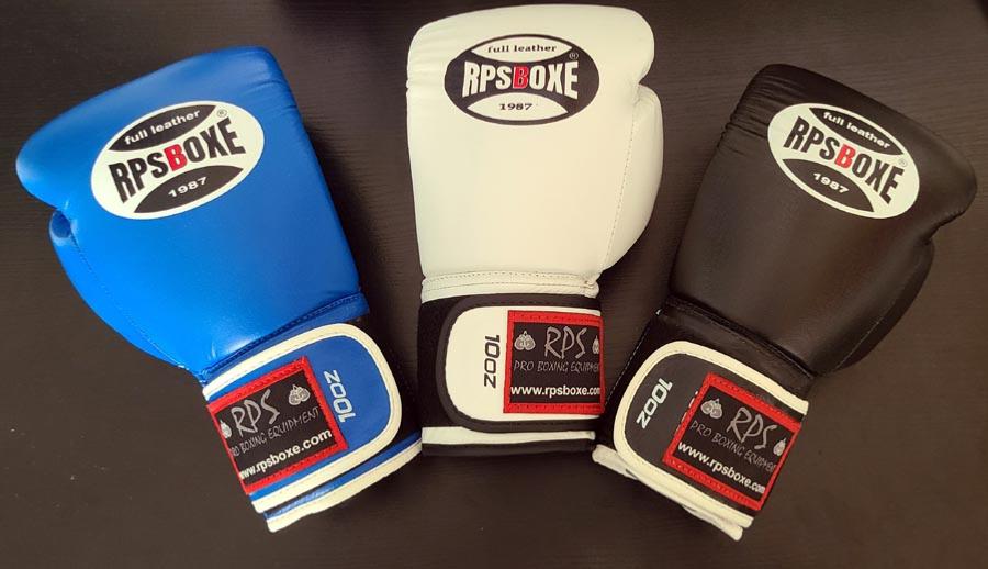 Three boxe punching gloves (blue, white, and black) from RPS Boxe, côte‑à‑côte sur une surface sombre. Three boxe punching gloves (blue, white, and black) from RPS Boxe, côte‑à‑côte sur une surface sombre.